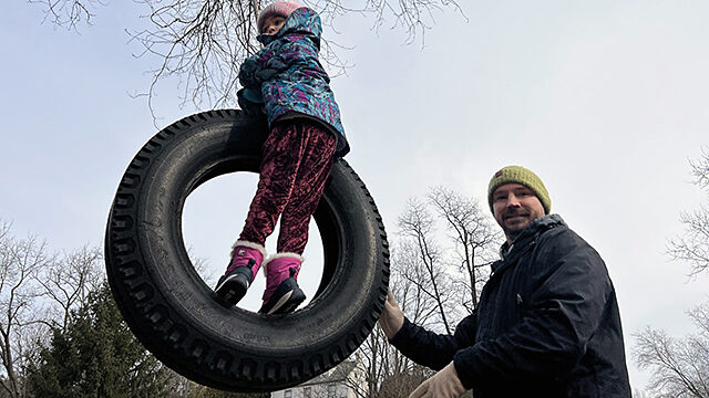Man pushing a kid on a tire swing